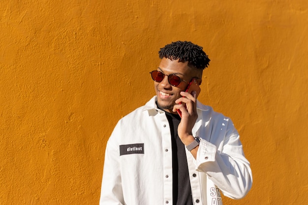 Retrato de un joven negro latino con gafas de sol hablando por teléfono y sonriendo con un fondo amarillo