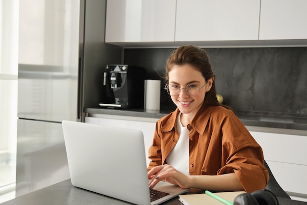 Foto retrato de una joven nómada digital freelance que trabaja desde casa usando una computadora portátil y usando gafas