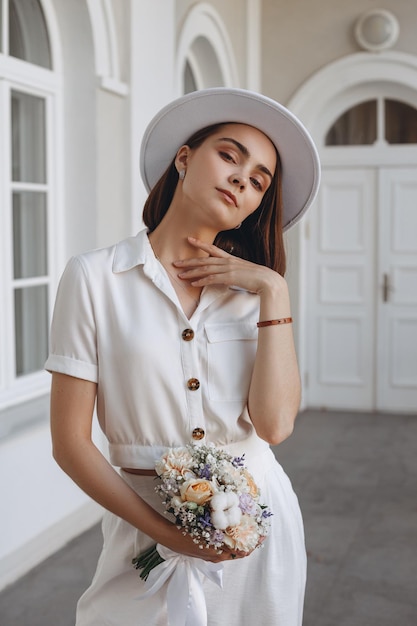 Retrato de una joven novia elegante con un traje de boda moderno con ramo de flores en el balcón