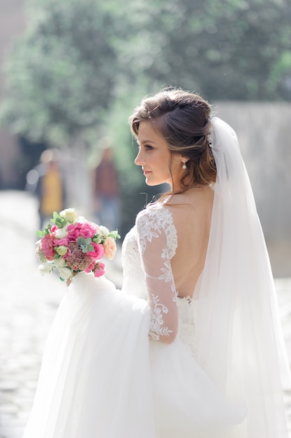 Retrato de una joven novia hermosa en la ciudad vieja. En manos de una niña con un ramo de novia.