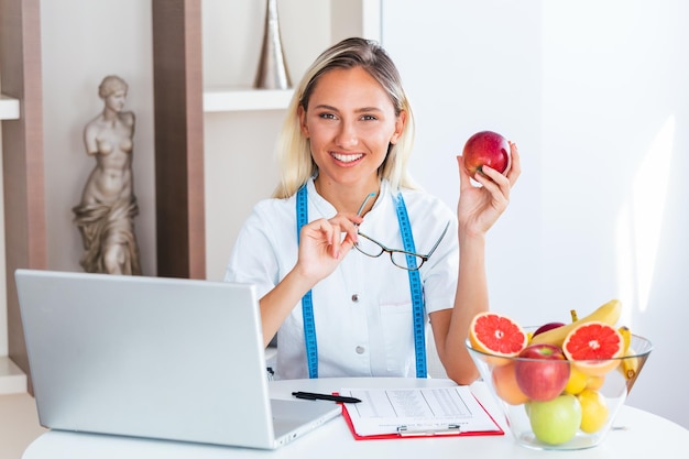 Foto retrato de una joven nutricionista sonriente en la sala de consulta mesa de nutricionista con jugo de frutas saludable y cinta métrica dietista trabajando en un plan de dieta