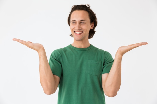 Retrato de joven optimista vistiendo camiseta básica riendo y gesticulando con las manos a un lado aislado sobre la pared blanca