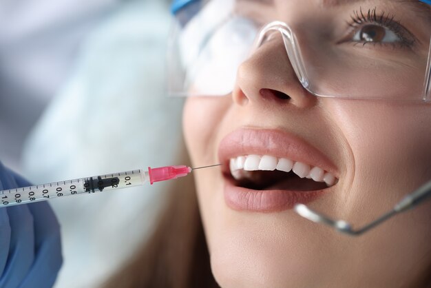 Retrato de joven paciente sentada en la silla del dentista con la boca abierta y recibiendo una inyección ...