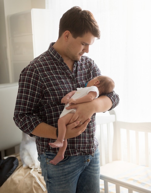 Retrato de joven padre con bebé recién nacido en manos en casa