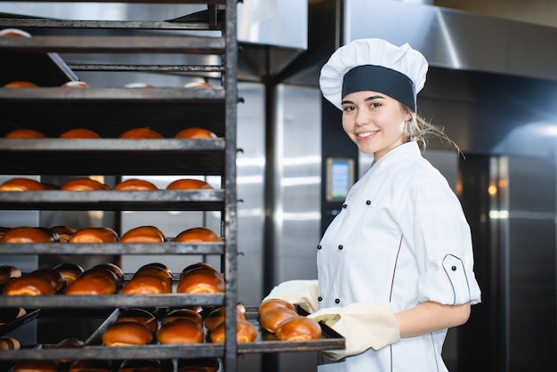 Retrato de una joven panadera con horno industrial con pasteles en una panadería