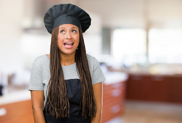 Retrato de una joven panadera negra mirando hacia arriba, pensando en algo divertido y teniendo una