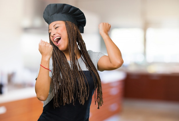 Retrato de una joven panadera negra muy feliz y emocionada, alzando los brazos.