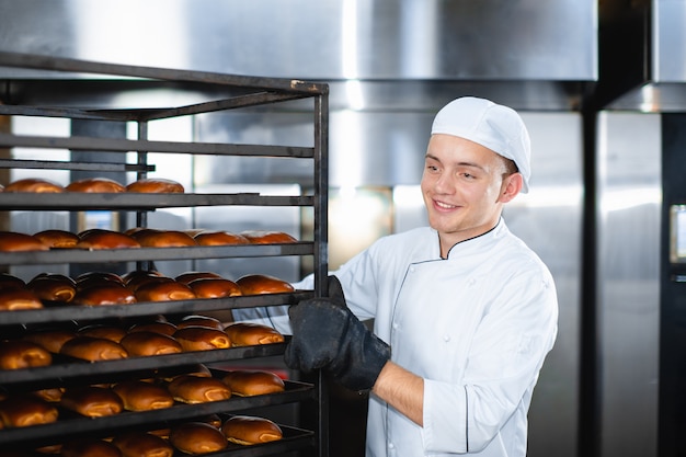 Retrato de un joven panadero con horno industrial con pasteles en una panadería