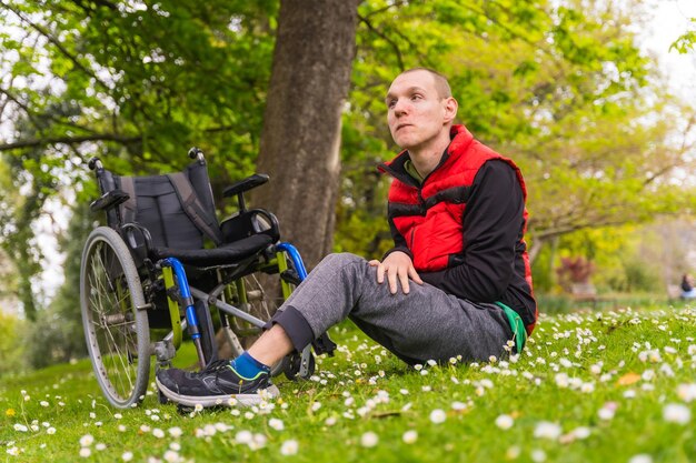 Retrato de un joven paralizado sentado en el césped junto a la silla de ruedas una margarita florece en primavera en un parque natural