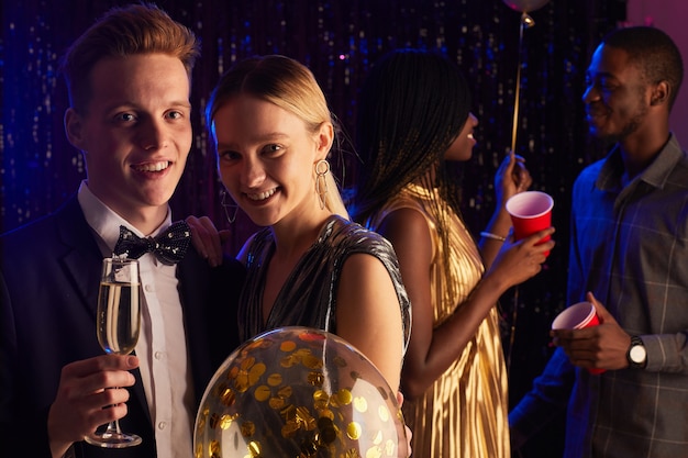 Retrato de joven pareja de adolescentes sonriendo a la cámara mientras disfruta de la noche de graduación, espacio de copia