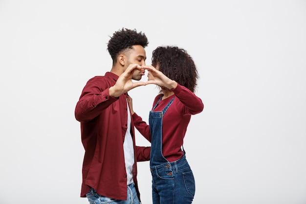 Retrato de una joven pareja africana sonriente abrazando y mostrando el gesto de corazón con los dedos.