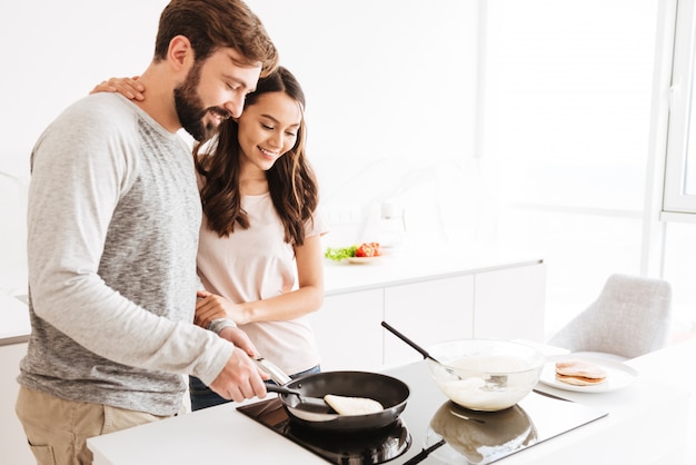 Retrato de una joven pareja alegre cocinar panqueques