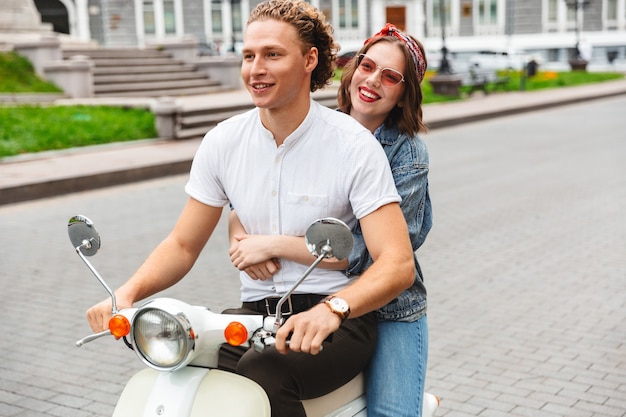 Foto retrato de una joven pareja alegre montando en una moto juntos en las calles de la ciudad