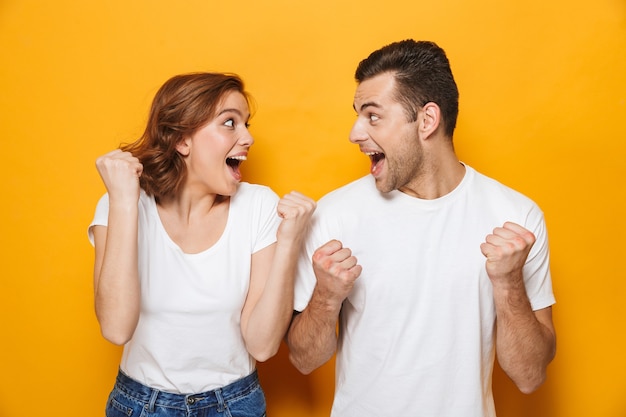 Foto retrato de una joven pareja alegre que se encuentran aisladas sobre la pared amarilla, celebrando el éxito