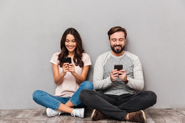 Foto retrato de una joven pareja alegre usando teléfonos móviles