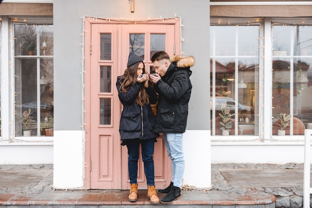 Retrato de una joven pareja amorosa feliz de pie cerca de la cafetería al aire libre tomando café.