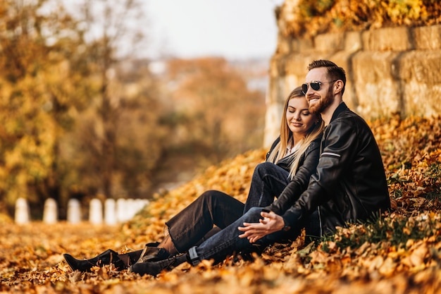 Retrato de una joven pareja amorosa, sentada en la hoja de otoño y disfrutando de la naturaleza