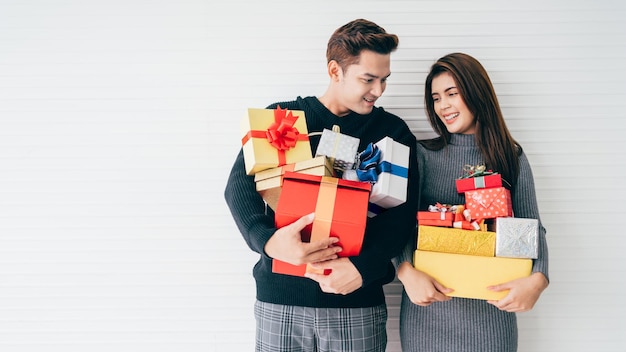 Retrato de una joven pareja asiática emocionada y sorprendida sosteniendo muchas cajas de regalo apiladas en sus manos con fondo blanco Concepto de banner publicitario de Navidad y año nuevo Imagen con espacio de copia