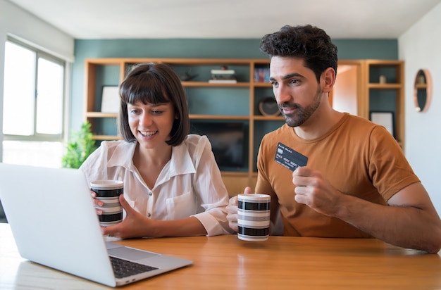 Retrato de joven pareja de compras en línea con una tarjeta de crédito y una computadora portátil desde casa.