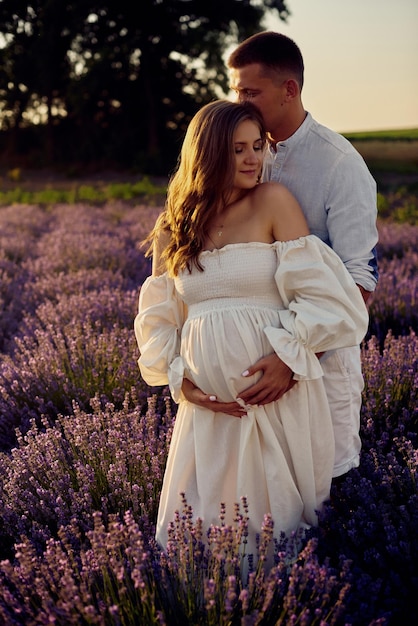 Retrato de una joven pareja embarazada hermosa en un campo de lavanda al atardecer Concepto de familia feliz