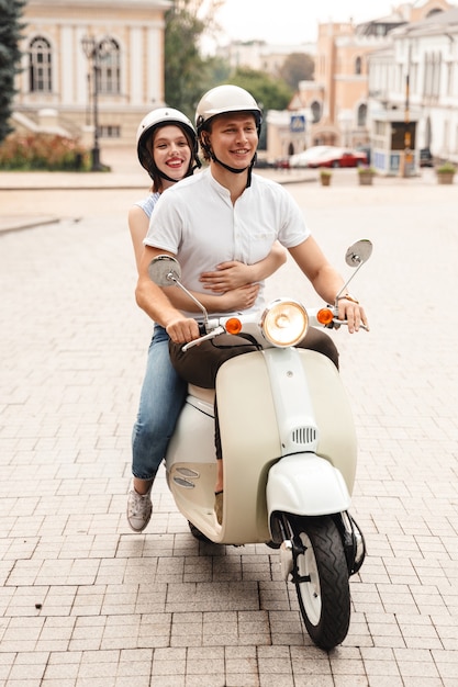 Retrato de una joven pareja feliz en cascos montando en una moto juntos en la calle de la ciudad