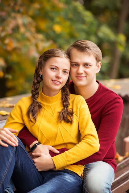 Retrato de una joven pareja feliz en coloridos suéteres en un parque de otoño