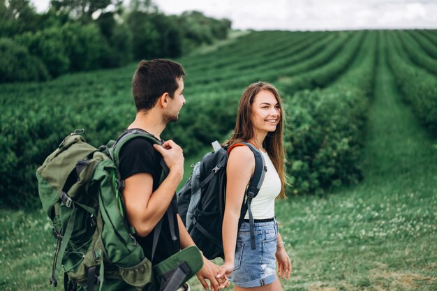 Retrato de la joven pareja feliz con mochilas en el campo en primavera. Hombre y mujer caminando en plantaciones de grosellas