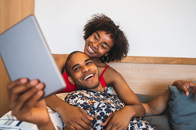 Retrato de joven pareja latina tomando un selfie con tableta digital en casa. Concepto de tecnología y estilo de vida.