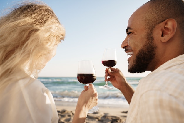 Retrato de una joven pareja sentada en la playa y bebiendo vino