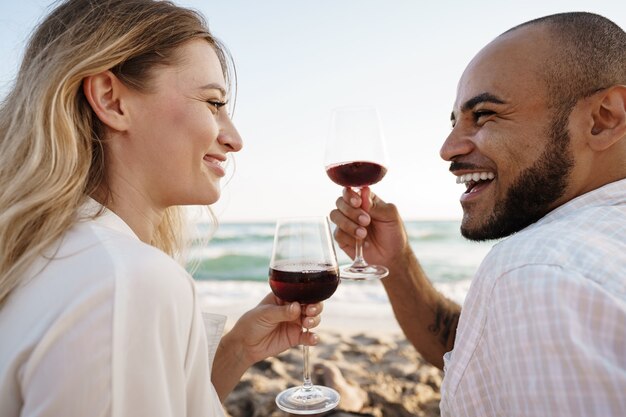 Foto retrato de una joven pareja sentada en la playa y bebiendo vino