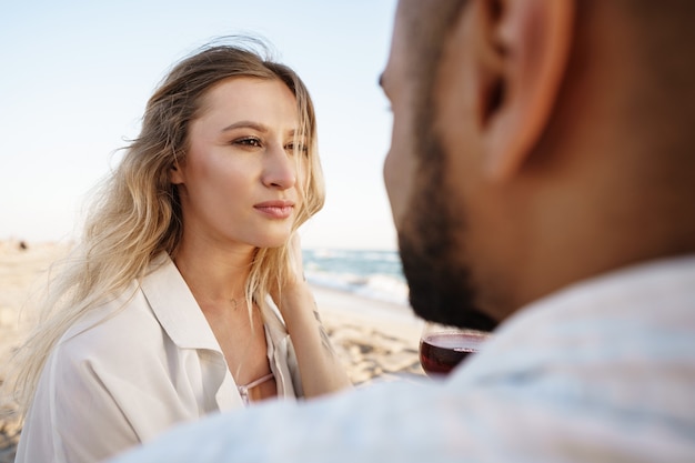 Retrato de una joven pareja sentada en la playa y bebiendo vino