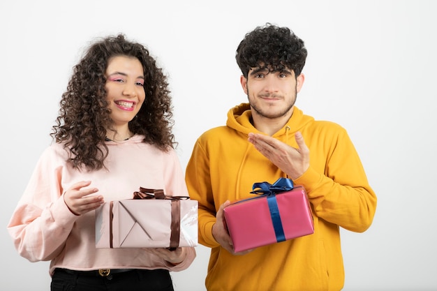 Retrato de joven pareja sosteniendo cajas de regalo sobre pared blanca.