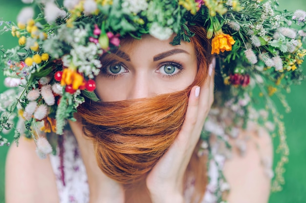 Retrato de una joven pelirroja con una corona de flores en la cabeza, en el contexto de la naturaleza.