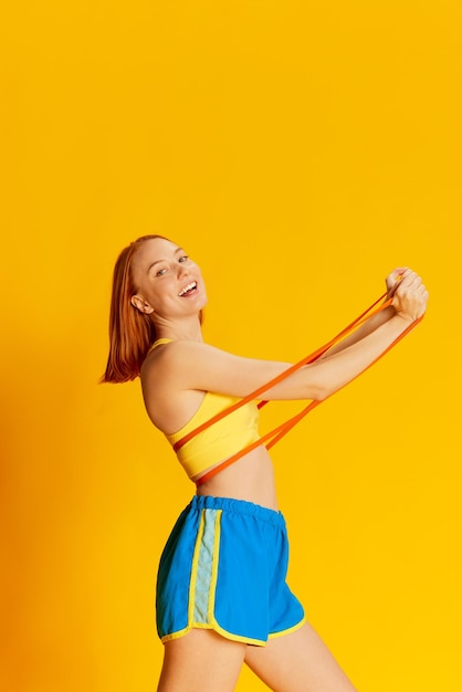 Retrato de joven pelirroja en entrenamiento de ropa deportiva con equipo deportivo sobre fondo amarillo Ejercicios de manos con expansor