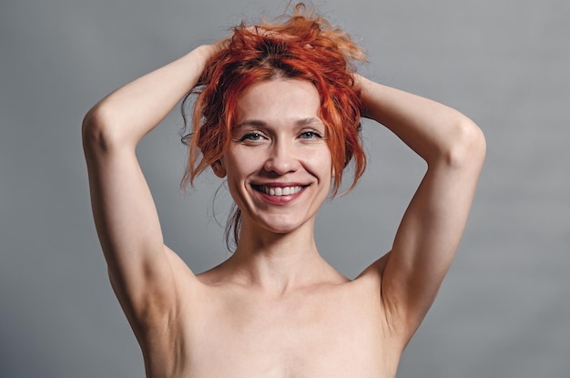 Retrato de una joven pelirroja con una linda sonrisa Hombros desnudos manos detrás de su cabeza Sexualidad