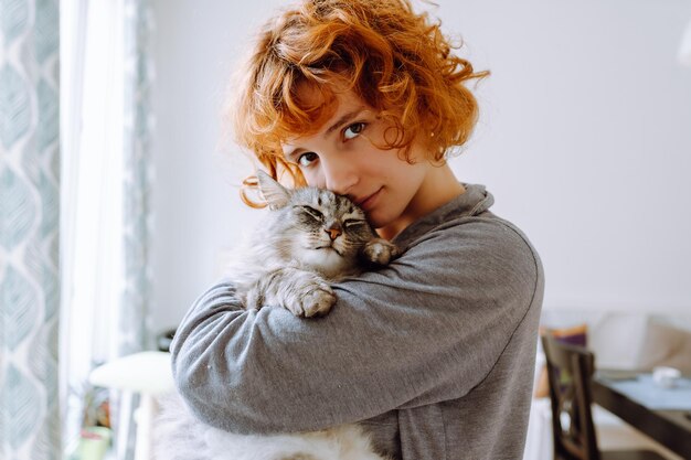 Foto retrato de una joven pelirroja rizada con su amado gato doméstico esponjoso