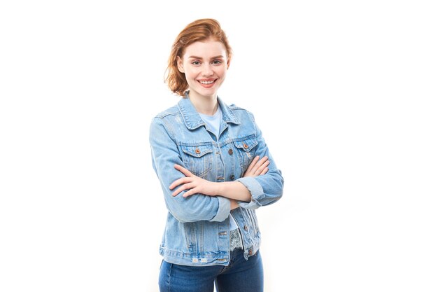 Retrato de una joven pelirroja sobre un fondo blanco aislado en jeans. Mira a la cámara
