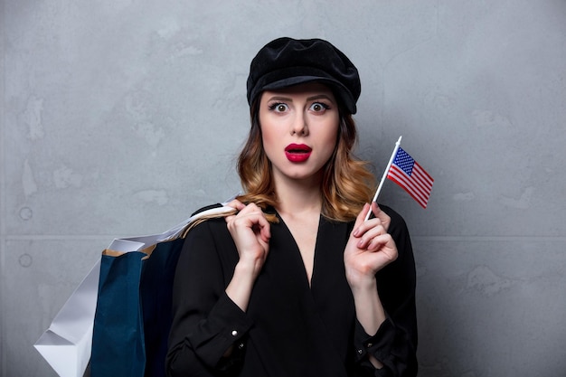 Retrato de joven pelirroja vestida de negro con bolsas de compras y bandera de los Estados Unidos sobre fondo gris