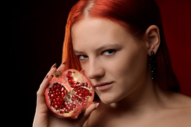 Retrato de una joven con pelo rojo y fruta de granada en manos