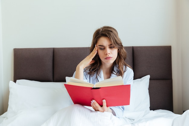 Retrato de una joven pensativa en pijama leyendo libro