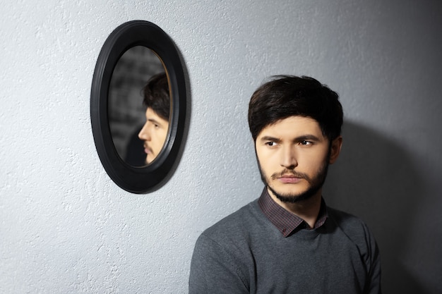 Retrato de joven pensativo cerca de su reflejo en el espejo negro ovalado