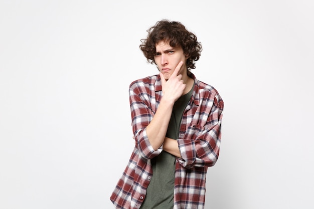 Retrato de joven pensativo sospechoso en ropa casual mirando a cámara, poner apoyo de la mano en la barbilla aislada sobre fondo de pared blanca. Personas sinceras emociones, concepto de estilo de vida. Simulacros de espacio de copia.