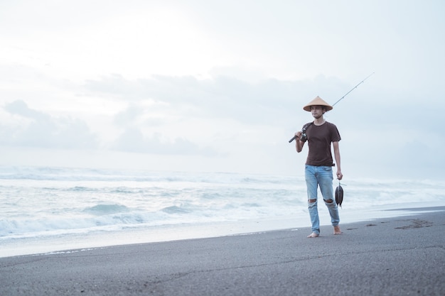 Retrato de un joven pescador caminando solo sosteniendo peces capturados en la playa