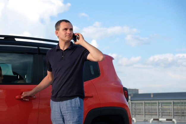 Retrato de un joven de pie cerca de un coche hablando por teléfono