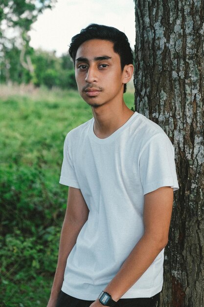 Foto retrato de un joven de pie contra un árbol