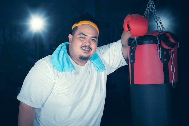 Foto retrato de un joven de pie junto al saco de boxeo por la noche