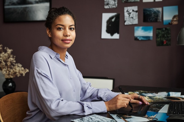 Retrato de una joven positiva que usa una tableta gráfica al editar fotos para el cliente