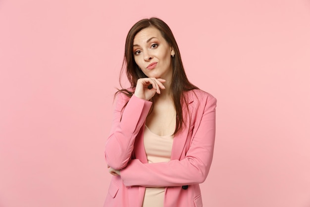 Retrato de una joven preocupada con chaqueta que puso la mano en la barbilla con una cámara aislada en un fondo rosa pastel en el estudio. Emociones sinceras de la gente, concepto de estilo de vida. Simulacros de espacio de copia.