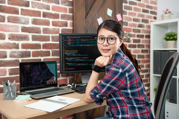 Foto retrato de una joven programadora asiática sentada en su oficina de trabajo y sonriendo amablemente.