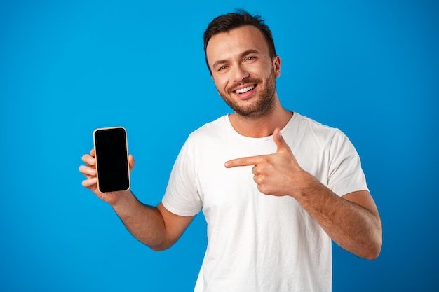 Foto retrato de joven publicidad nuevo smartphone mostrándolo a la cámara contra el fondo azul.